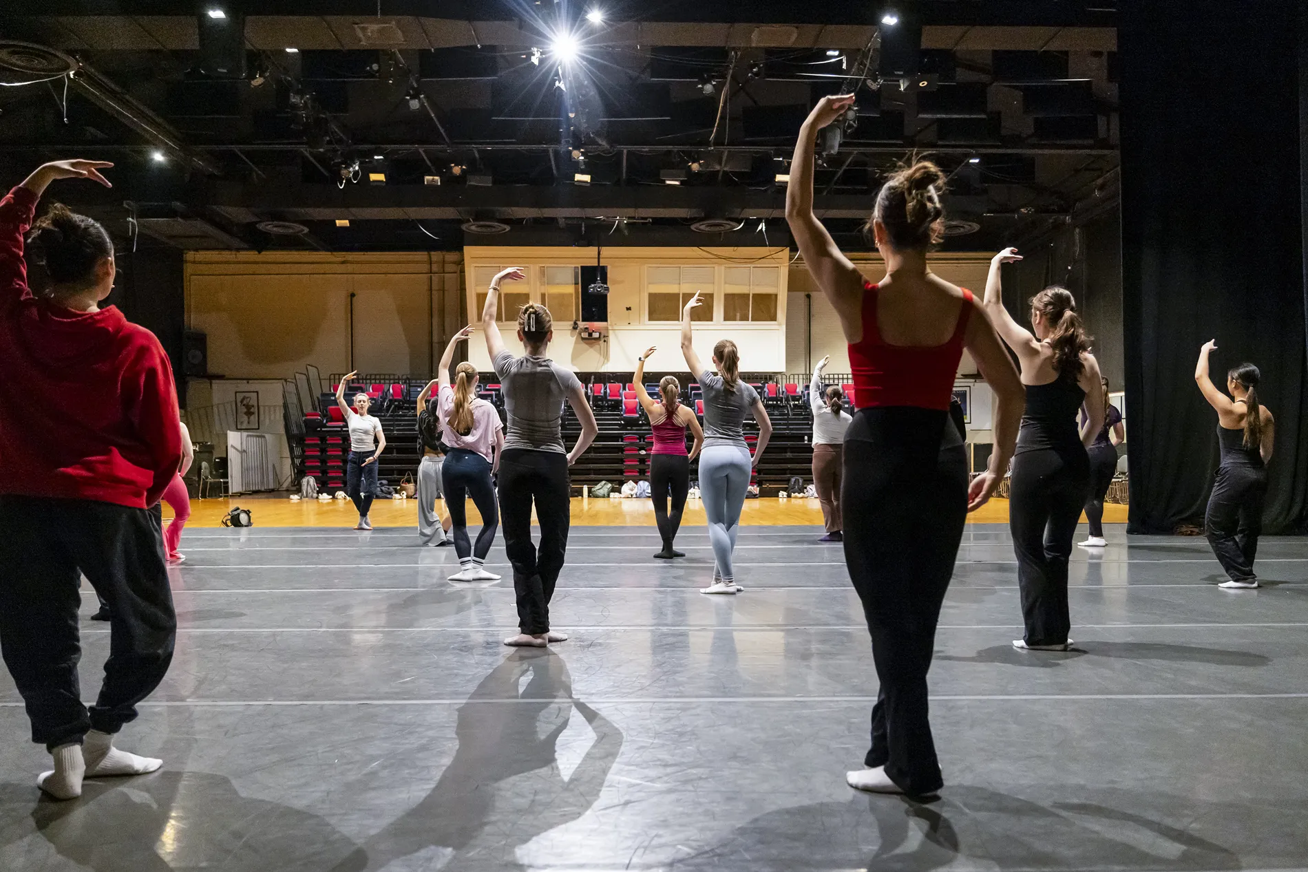 A classroom of dancers at the UGA department of dance pose with their feet close together and one arm above their heads.