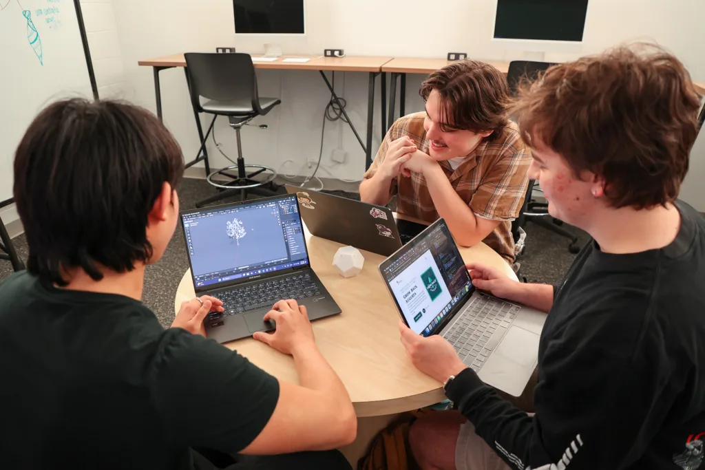 Three students sit around a table with laptops while discussing the Grow Back Project.