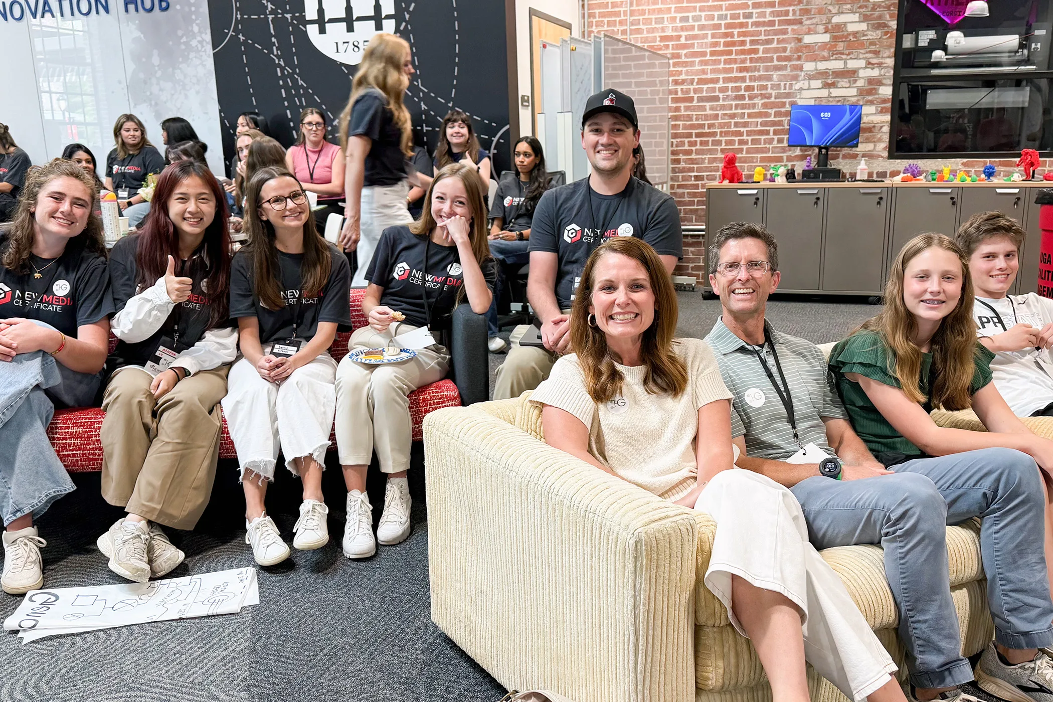 Candace Couch and her family pose with New Media Institute students in a classroom space.