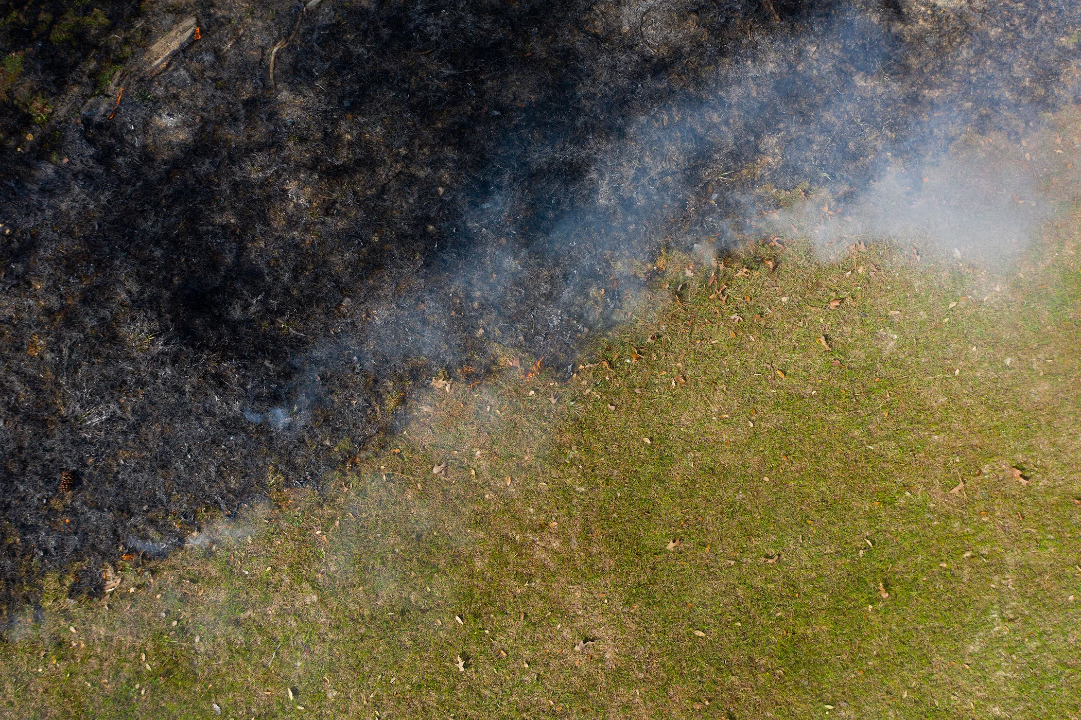 Overhead aerial view of the underbrush smoldering next to untouched grass at the end of a burn exercise during a prescribed burn.