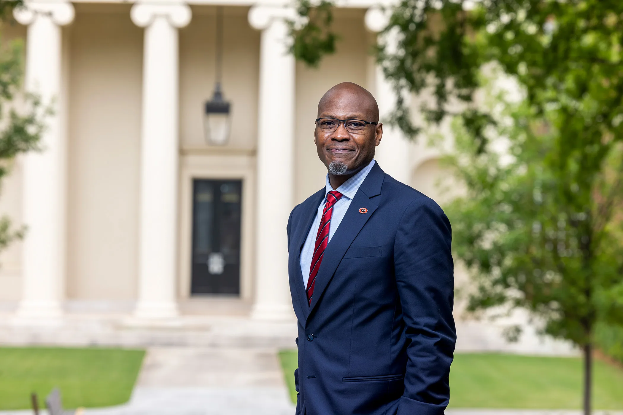 Ron Walcott in a navy suit poses outside a columned campus building.