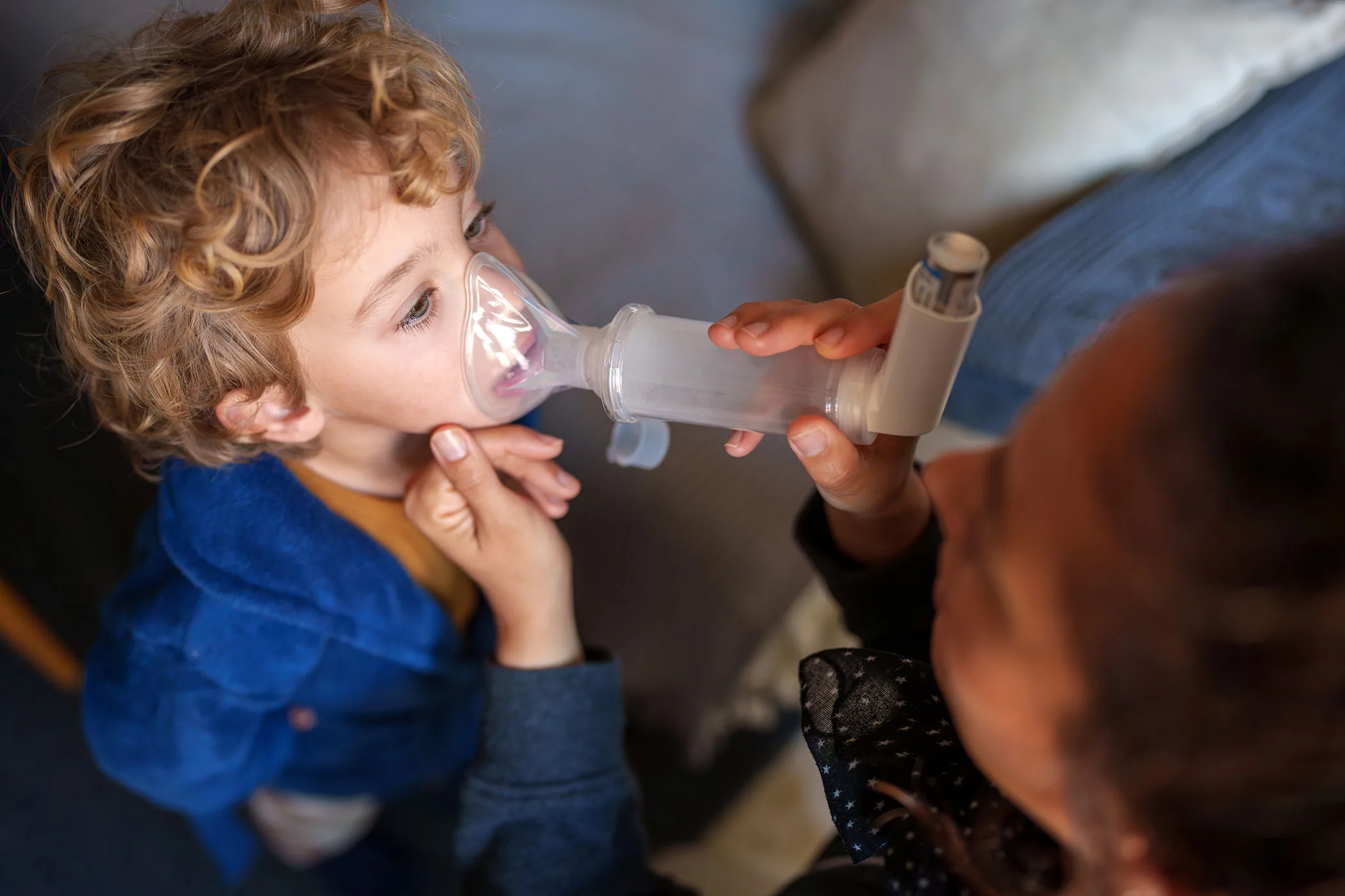 Child receives asthma medication using a spacer and inhaler with an adult's help.