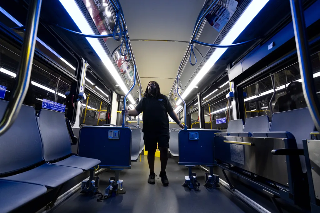 A man walks along the inside of a darkened bus with blue seats.
