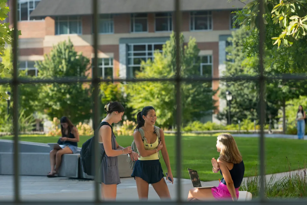 Students in a college courtyard can be seen through a blurry window.