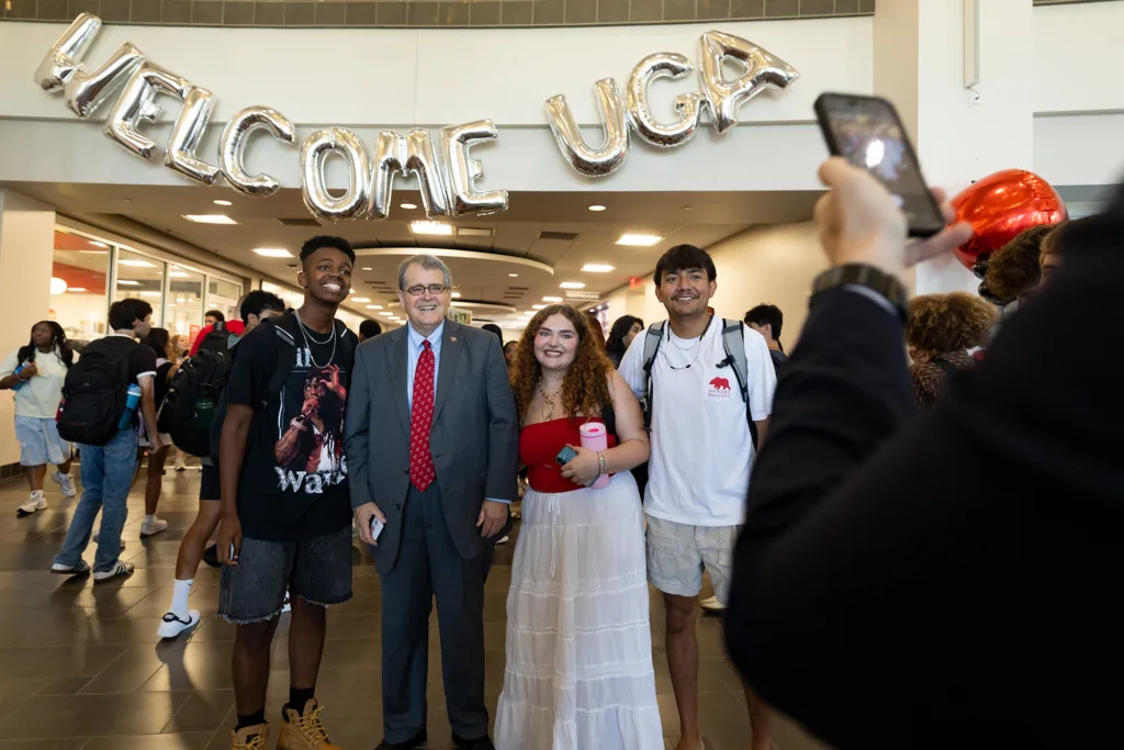 Four people pose for a photo. They stand under letter-shaped balloons that spell “Welcome UGA.”