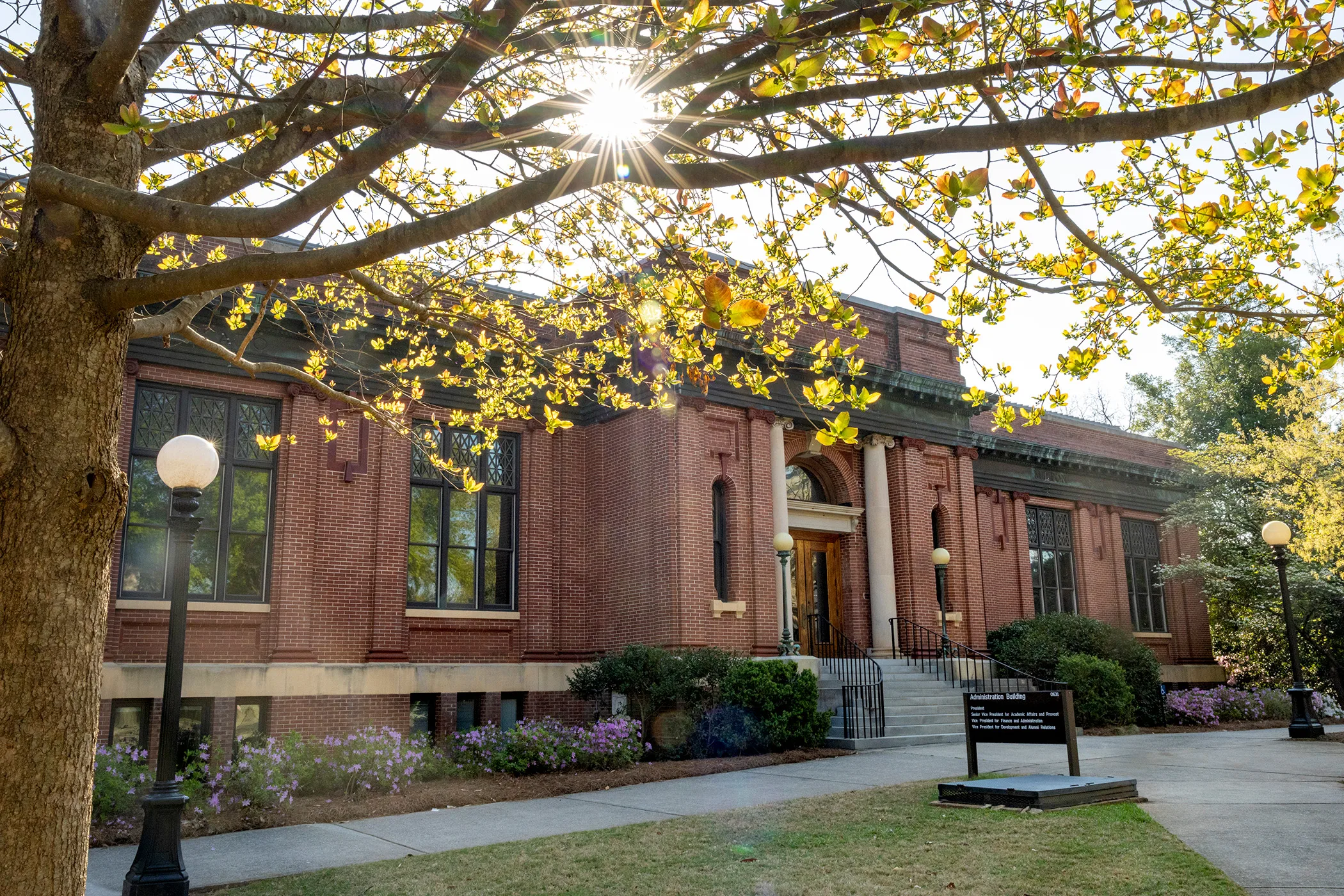 Sunlight shines through trees surrounding a brick campus building.