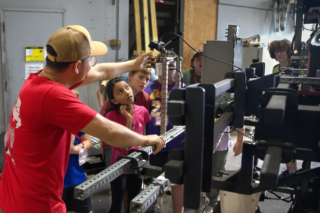 A man shows a group of students how to operate a piece of technology.