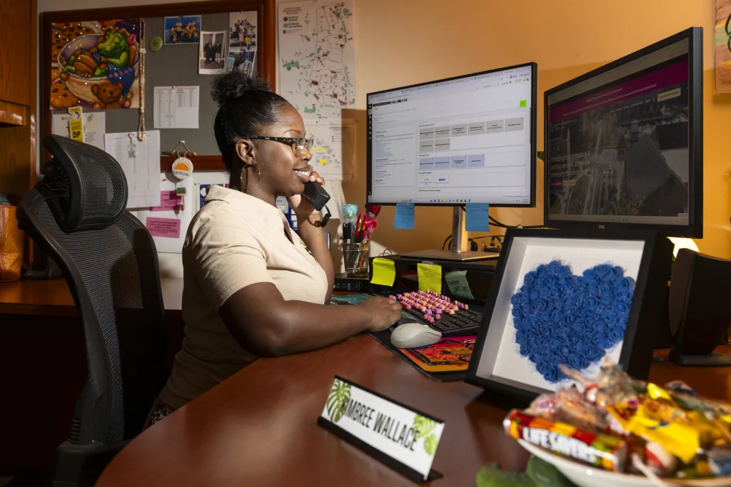 A woman takes a call at her desk while working on a computer