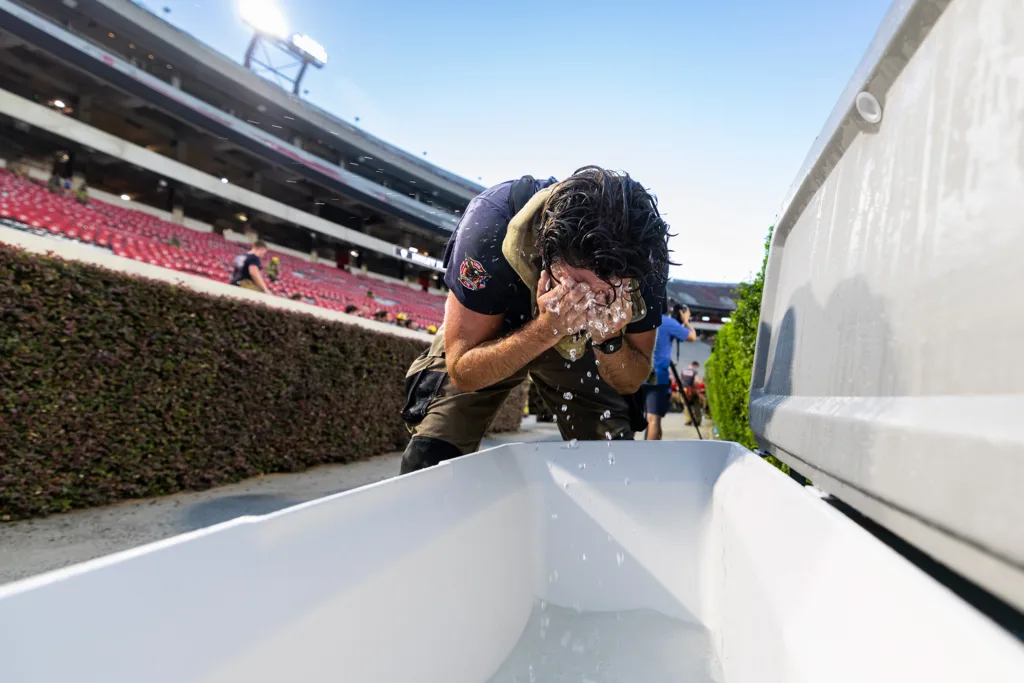 A man splashes his face with water from a white cooler.