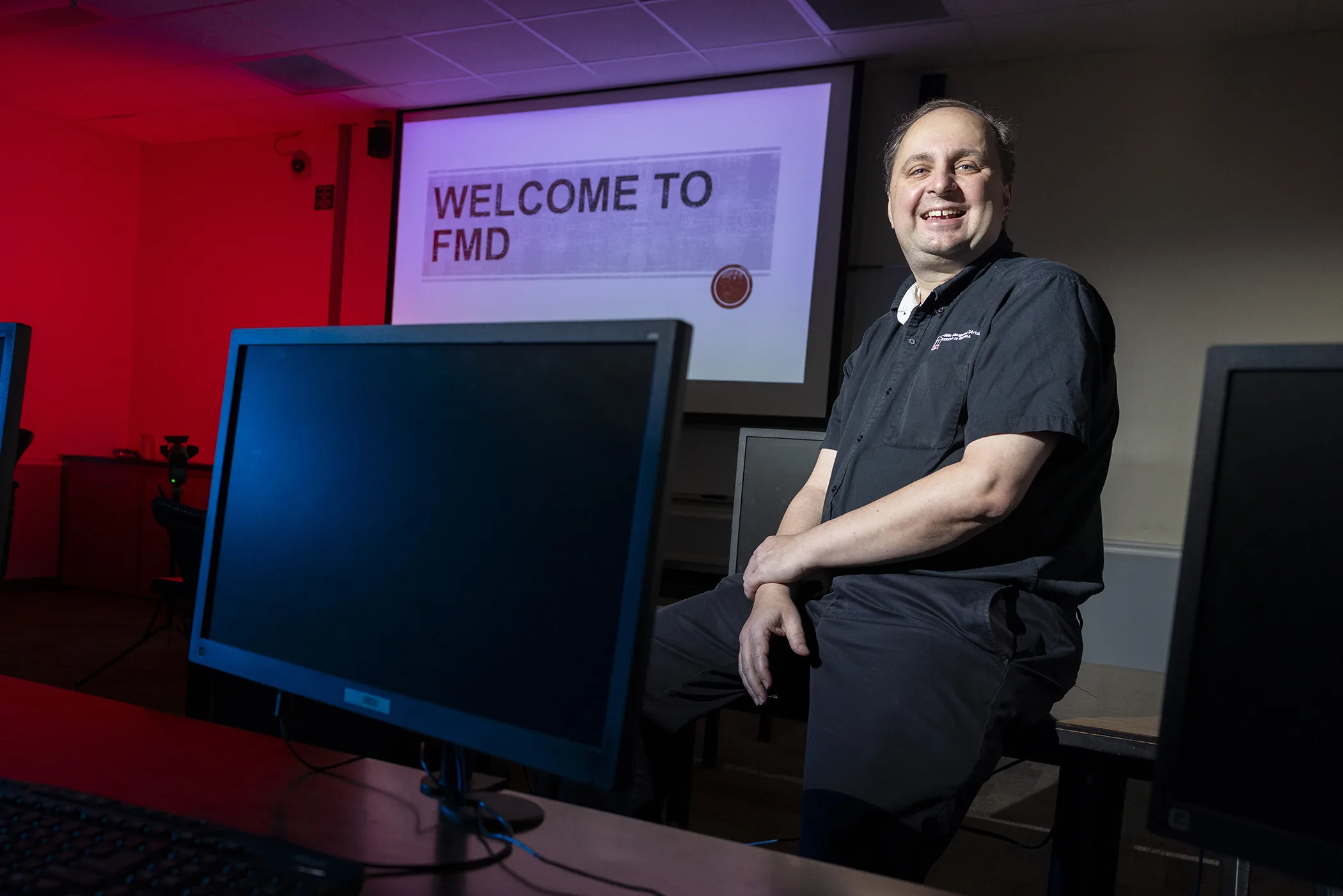 Man sits on a table between computers in front of a presentation.