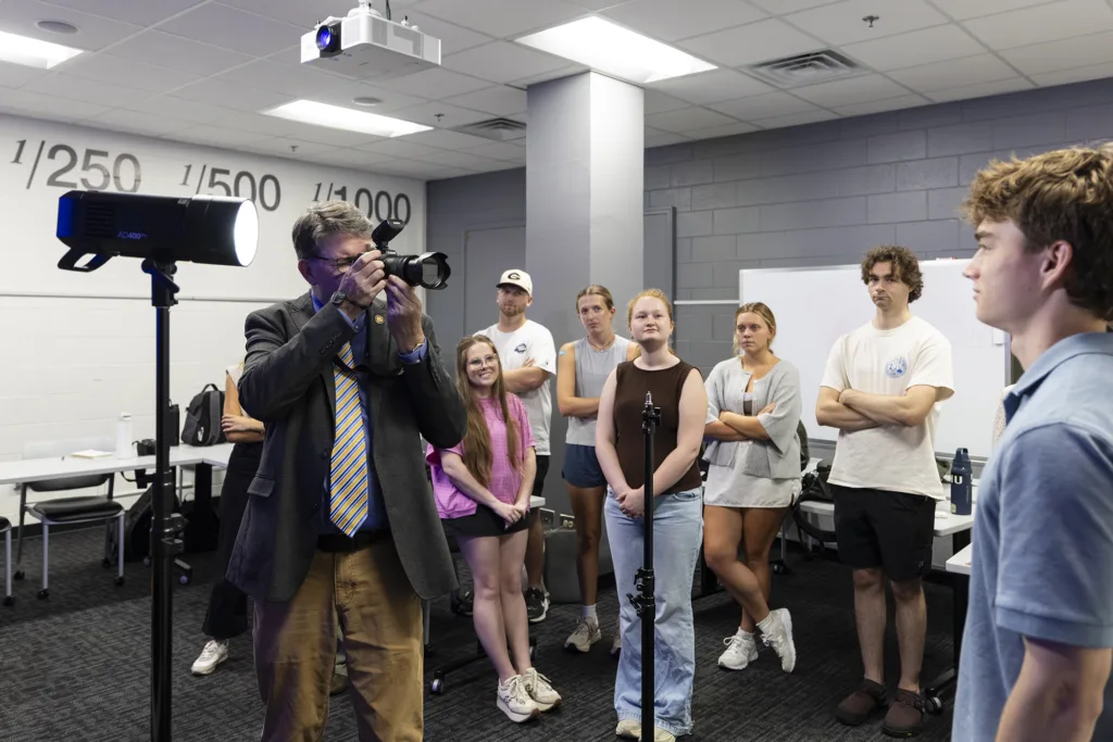 Man takes a picture of one of his students while other students watch.